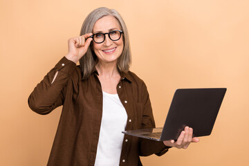 Portrait of good mood clever person with bob hairstyle wear stylish jacket hold laptop touching glasses isolated on beige color background