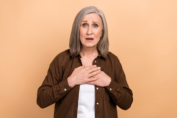 Fototapeta Photo of worried impressed aged lady arms touch chest staring cant believe isolated on beige color background obraz