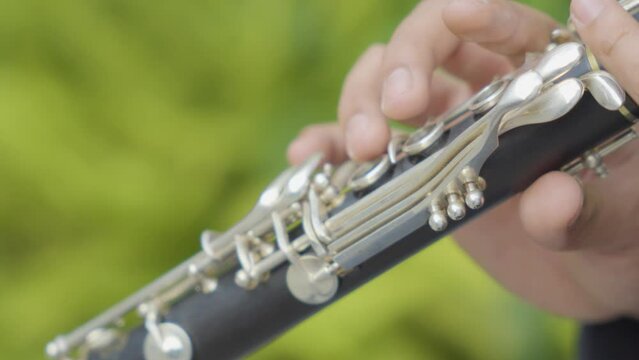 Close Up of a Man's Fingers Playing a Clarinet with Green Blurred Background.