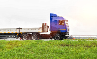 A truck with a semi-trailer transports cargo in the summer on a motorway in rainy weather. Copy space for text