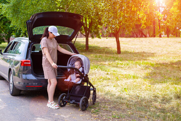 A beautiful girl puts a baby stroller into the open trunk of a car. Traveling in a family car. Copy...