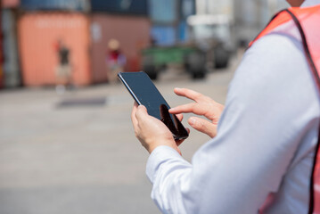Technology concept, A man, shipping worker touching smart phone screen to manage an online order at the container dock, stock, freight and cargo supply chain logistics