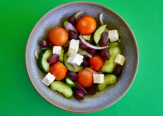 A bowl of Greek salad against a green background