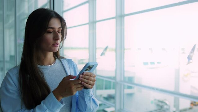 Attractive cute busy Caucasian woman sitting at airport waiting for flight looking at smartphone using online. Beautiful successful girl checking social media during traveling. Airport concept.