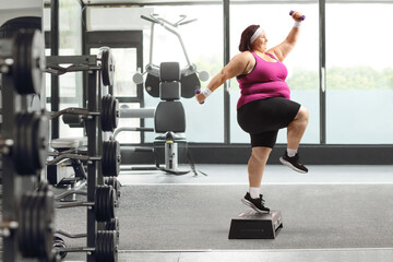 Fototapeta na wymiar Overweight woman exercising in a gym and jumping on a step aerobic platform