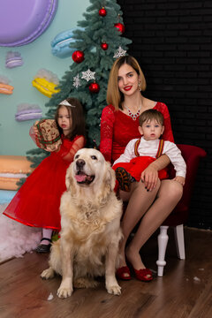 Family photo portrait. Mom and her two children and a white dog in red clothes celebrate the Chistmas, new year. Happy young mother and her daughter, son and a dog in a cozy dark living room on