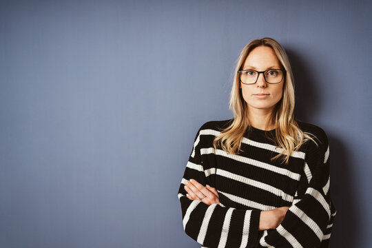 Serious Young Woman with Glasses Standing in Front of Blue Wall and Looking into the Camera with Copy Space
