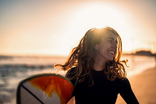 Portrait of female surfer with surfboard at sunset.