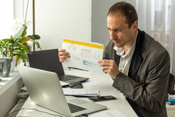 Naklejka premium Frustrated dazed caucasian man, company employee, product manager, ceo, sitting at workplace in the office, looking at financial documents in surprise, dissatisfied with the result of work