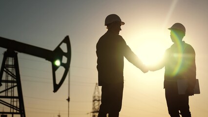 oil business. workers of the fuel industry shaking hands with oil pumps on the lifestyle...