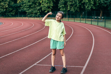 Strong little girl posing outdoors showing their muscles.