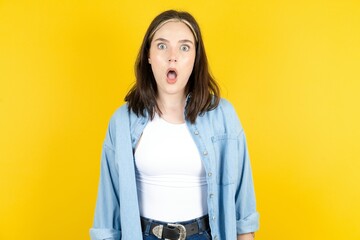 Oh my God. Surprised Young beautiful woman wearing denim overshirt stares at camera with shocked...