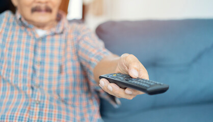 Midsection of senior man using TV remote control while sitting on couch in nursing home.