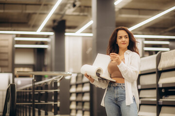 Young woman choose wallpaper in hardware store. Home design and renovation concept.