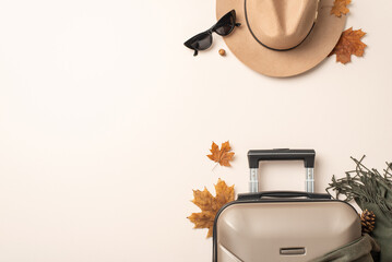 Autumnal elegance meets travel chic. Top view of a felt hat, cat-eye sunglasses, scarf, suitcase, maple leaves on a neutral backdrop with empty space for text