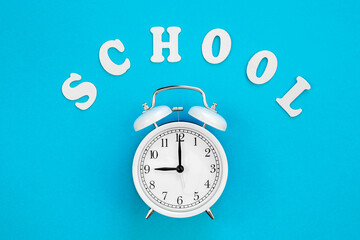 Alarm clock and the word school on a blue background, top view.