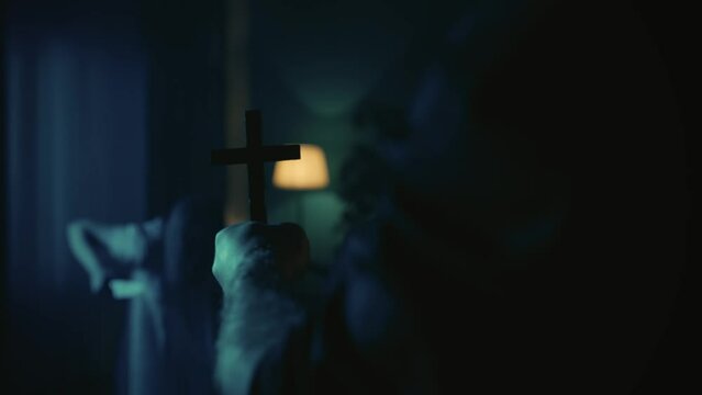 Video of a priest approaching a possessed female, ghost, entity with a knife in hand. The exorcist holds a cross in hand, shaking, scaring the paranormal creature away.