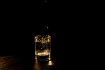 Glass of water with effervescent soluble tablet on dark background