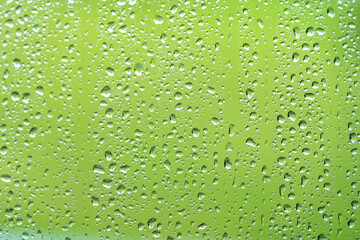 Drops of rain on window with green background.