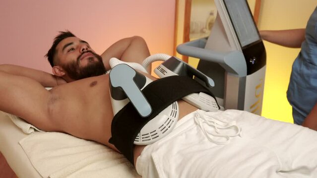 Male mexican latin handsome beard model at spa wellness center hotel begin therapy of EMS electro muscle stimulation in the abdomen abs and smile to therapist