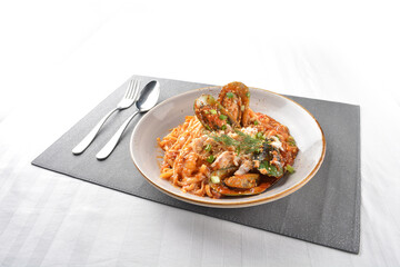 seafood pasta with big tiger prawn, scallop shell clam and muscle in spicy chilli crab tomato paste sauce in plate on white marble table western spaghetti cuisine halal food hotel luxury cafe menu