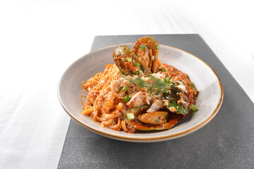 seafood pasta with big tiger prawn, scallop shell clam and muscle in spicy chilli crab tomato paste sauce in plate on white marble table western spaghetti cuisine halal food hotel luxury cafe menu