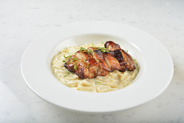 stir fried carbonara pasta noodle with grilled bbq teriyaki chicken chop in creamy cheese white milk sauce in plate on white table western spaghetti cuisine halal food hotel luxury cafe menu