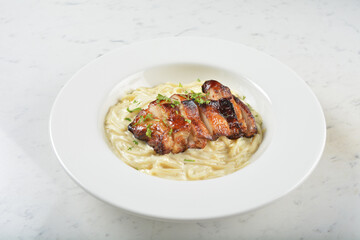 stir fried carbonara pasta noodle with grilled bbq teriyaki chicken chop in creamy cheese white milk sauce in plate on white table western spaghetti cuisine halal food hotel luxury cafe menu