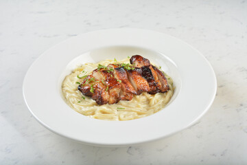 stir fried carbonara pasta noodle with grilled bbq teriyaki chicken chop in creamy cheese white milk sauce in plate on white table western spaghetti cuisine halal food hotel luxury cafe menu
