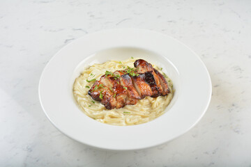 stir fried carbonara pasta noodle with grilled bbq teriyaki chicken chop in creamy cheese white milk sauce in plate on white table western spaghetti cuisine halal food hotel luxury cafe menu