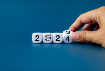 2024 New year business goal and trend concepts. End of 2023 to begin 2024 year numbers calendar with target dart icon on white cube blocks flipping by human hand isolated on blue banner background.