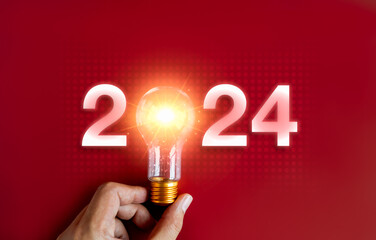 Shining 2024 calendar year numbers, neon style with creative trend light bulb holding by...