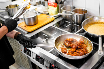 woman chef cooking chicken wings in a sauce on pan in the kitchen