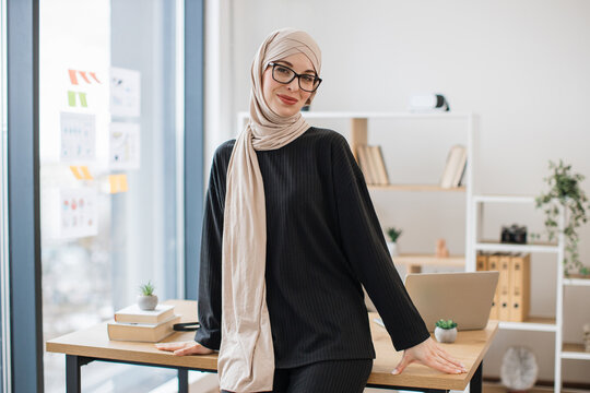 General manager in hijab leaning on desk in spacious office
