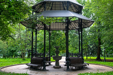 Openwork gazebo for relaxation with benches and a source of drinking water in the Mariinsky Park in...