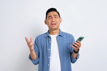 Unhappy young Asian man in casual shirt holding smartphone, receiving negative message, sad facial expression isolated on white background