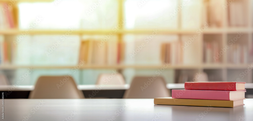 Poster white table with pile of books and chairs in the library with blurred bookshelves and sunshine in th