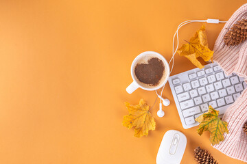 Autumn holidays cozy background, cozy flat lay with coffee latte cup with heart decor, computer laptop keyboard, earphones, warm sweater or plaid, fall leaves, on beige background top view copy space 