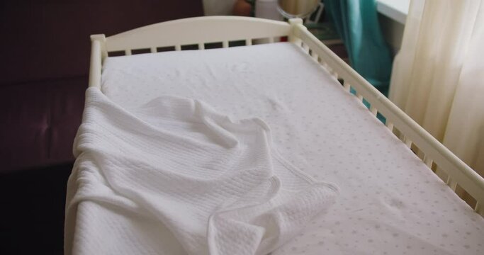 Modern empty wooden crib with mattress, cotton sheet and blanket in nursery room. Preparing baby bed for newborn comfort sleep.
