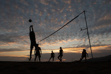 Gente jugando al voleibol en la playa al atardecer.