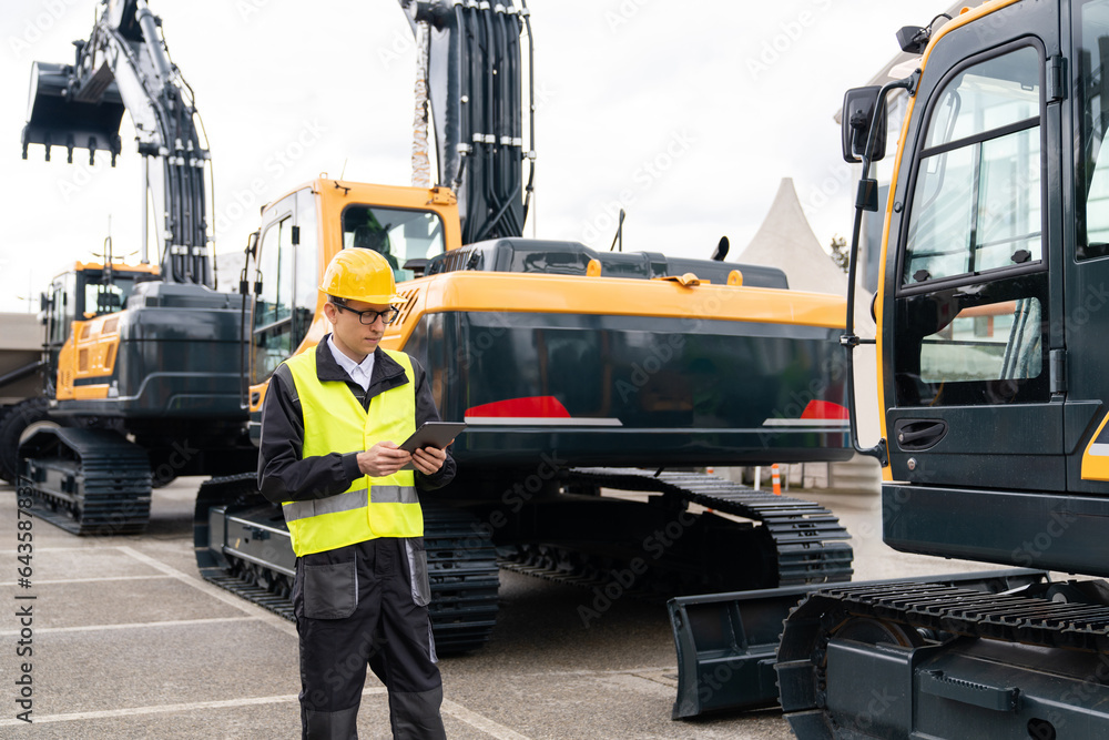 Aufkleber engineer in a helmet with a digital tablet stands next to construction excavators.