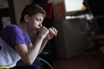 A teenage boy uses an allergy and asthma inhaler - obrazy, fototapety, plakaty