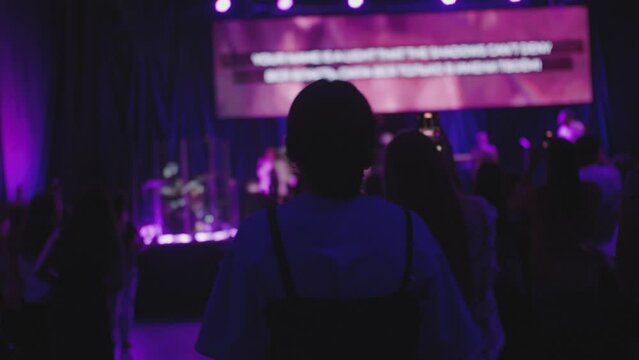 Christian Worship and Praise Music Night Concert. People Sing on Youth Festival or Conference Event with stage lights. Back view of unrecognizable female singing