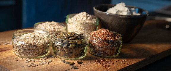 Cereals grains and pumpkin seeds portioned in glasses on rustic wooden board for a bread...