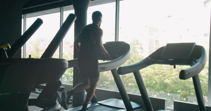 Athletic man run on treadmill at modern gym. Young sportsman doing cardio workout and jogging on running machine. Fitness and ealthy lifestyle concept