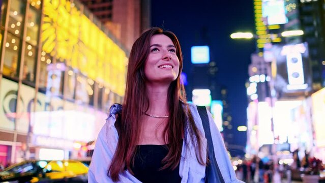 Portrait of joyful attractive Caucasian woman on Times Square, USA. Cute beautiful happy girl looking at buildings wearing stylish clothes with lots of people and cars on background.