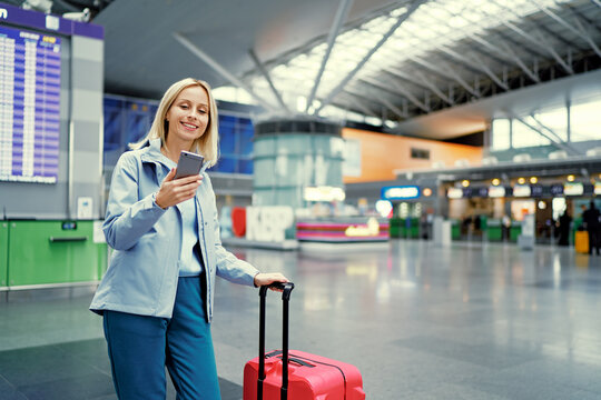 Travel and technology. Online check-in. Female traveler using smartphone waiting for boarding near registration desk line.