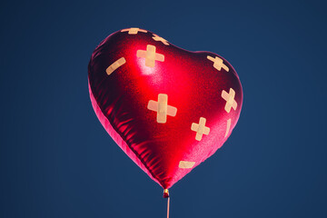 Red heart-shaped balloon fixed with bandaids. Broken heart remedy concept.