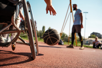 A physically challenged man in a wheelchair fearlessly engages in a spirited game of basketball with his supportive friends, breaking barriers and proving that passion and teamwork know no bounds. - obrazy, fototapety, plakaty