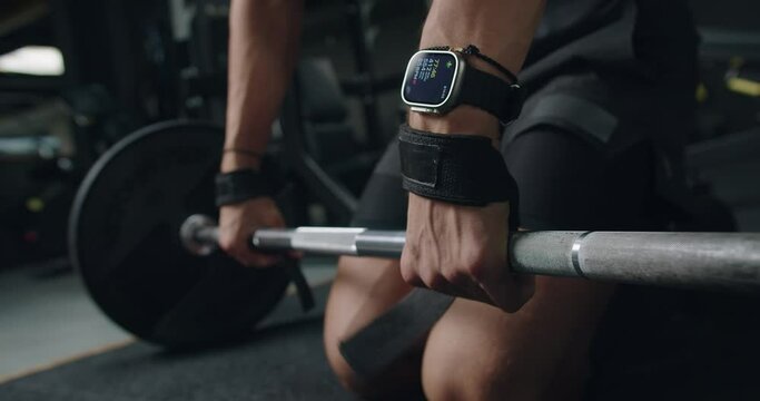Closeup of male hands in wrist lifting straps take barbell for exercising at gym. Cropped view on athletic man bodybuilder has workout at fitness club. Weightlifting and power training concept.